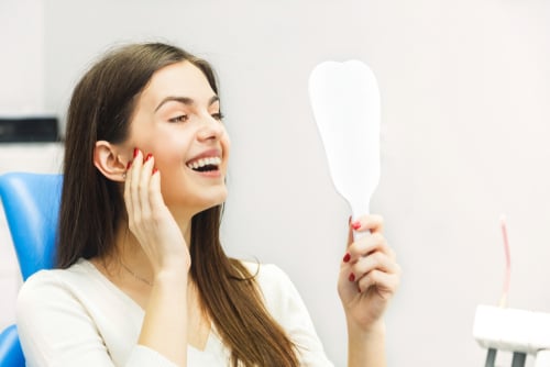 Smiling woman in a dental chair looking at her teeth in a handheld mirror